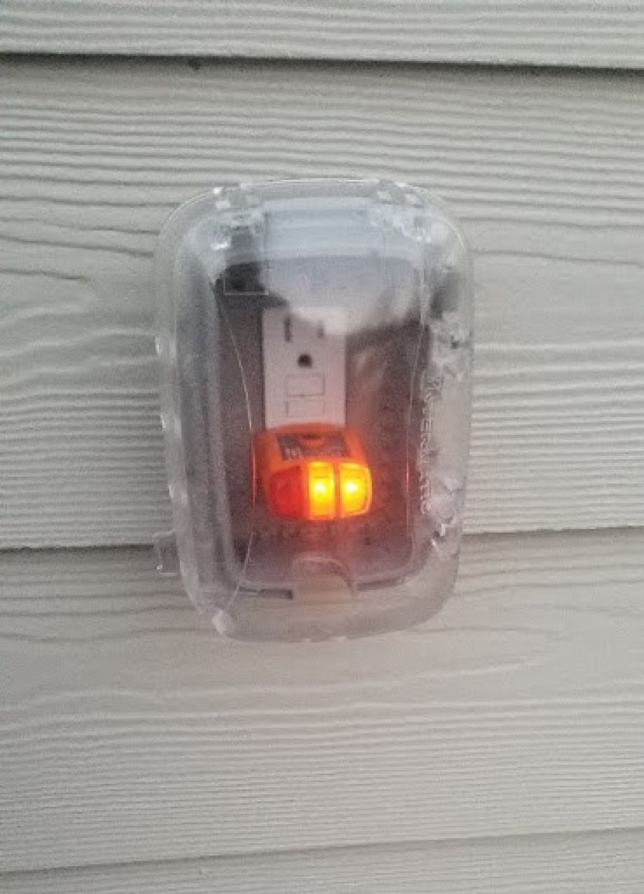 Outdoor GFCI outlet installed on house siding with a cover on it
