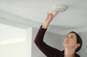 A woman testing a smoke detector.